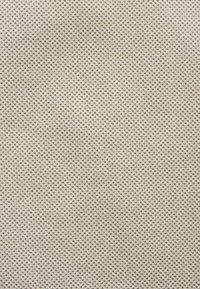 Tissu texturé de couleur beige clair présentant un subtil motif de petits points sombres, créant une apparence douce et tissée. Un matériau durable et flexible.