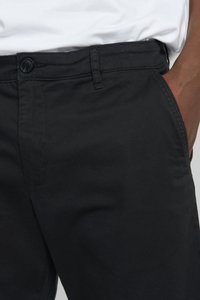 Černé bavlněné chinos kalhoty s knoflíkovým zapínáním, poutky na opasek a bočními kapsami. Hladký materiál s klasickým střihem a minimalistickým designem.