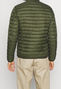 Giacca puffer verde oliva con motivo a righe orizzontali, colletto alto, polsini elastici e bordo nero all'orlo. Materiale leggero.