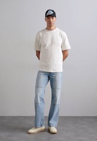 Gaiši beidzis īsām piedurknēm t-krekls, gaiši zili džinsi ar redzamām šuvēm, off-white sporta apavi un melna cepure ar zilu uzrakstu.