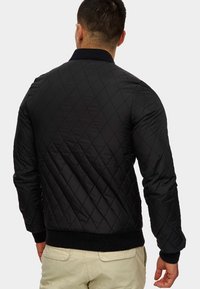 Czarna pikowana kurtka w rombowy wzór, z prążkowanymi mankietami i dołem. Gładki materiał, luźny krój i brak widocznych kieszeni.