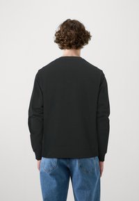 Sort sweatshirt med lange ærmer og rund hals, der har en glat tekstur og ribbede manchetter, parret med lyseblå denim jeans.