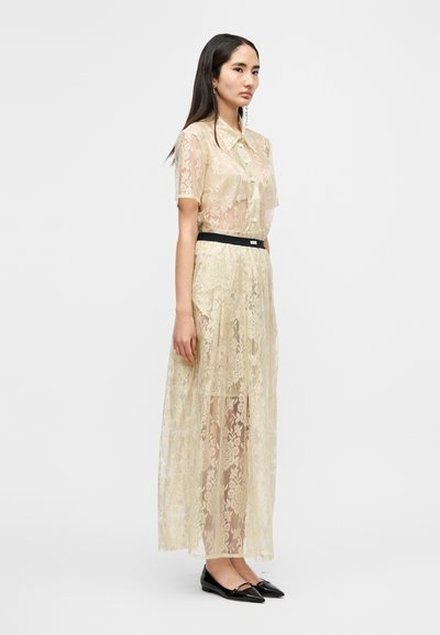 Μίντι φόρεμα από δαντέλα σε κρεμ απόχρωση, με γιακά σαν πουκάμισο, κοντά μανίκια και μαύρη ζώνη. Συνδυάζεται με μυτερές μαύρες μπαλαρίνες.