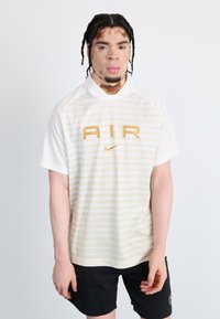White short-sleeve polo shirt with horizontal light yellow stripes, featuring a large gold 'AIR' logo and Nike swoosh. Black shorts.