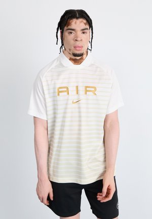 Weißes Poloshirt mit kurzen Ärmeln und horizontalen hellgelben Streifen, ausgestattet mit einem großen goldenen 'AIR'-Logo und Nike-Swoosh. Schwarze Shorts.