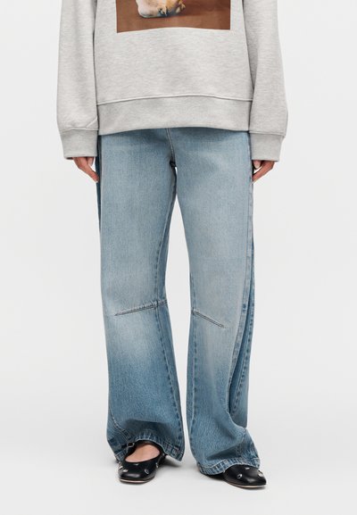 Τζιν φαρδιάς γραμμής σε ανοιχτό μπλε με ξεθωριασμένο πλύσιμο και διακριτικές ραφές, συνδυασμένα με γκρι φούτερ που φέρει γραφικό τύπωμα.