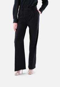 Schwarze taillierte Hose mit hoher Taille, weitem Beinprofil und vorderen Falten, gefertigt aus einem glatten Stoff, präsentiert mit einem schwarzen Oberteil.