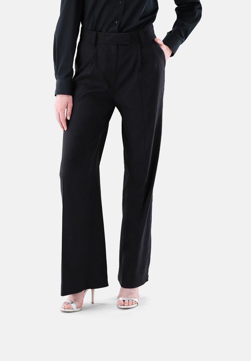 Schwarze taillierte Hose mit hoher Taille, weitem Beinprofil und vorderen Falten, gefertigt aus einem glatten Stoff, präsentiert mit einem schwarzen Oberteil.