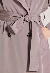 Lichtpaarse trenchcoat met een ceintuur in de taille, twee donkere knopen en zijzakken van een soepele stof.