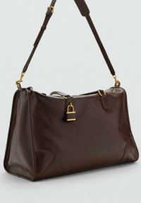 Sac à épaule en cuir marron foncé avec une sangle ajustable et détachable, des accessoires en or et un petit détail de cadenas sur un fond uni.
