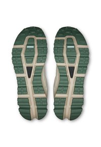Grüne und beigen Sneaker-Sohlen mit strukturiertem Gummi, ausgestattet mit hexagonalen Stollen für Traktion und einem zentralen schwarzen Detail auf jeder Sohle.