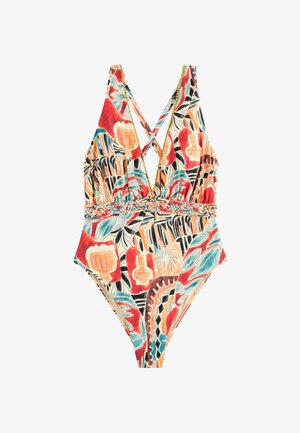 Femme aux longs cheveux foncés portant un maillot de bain une pièce coloré à motifs avec un profond décolleté en V, en extérieur sous lumière naturelle.
