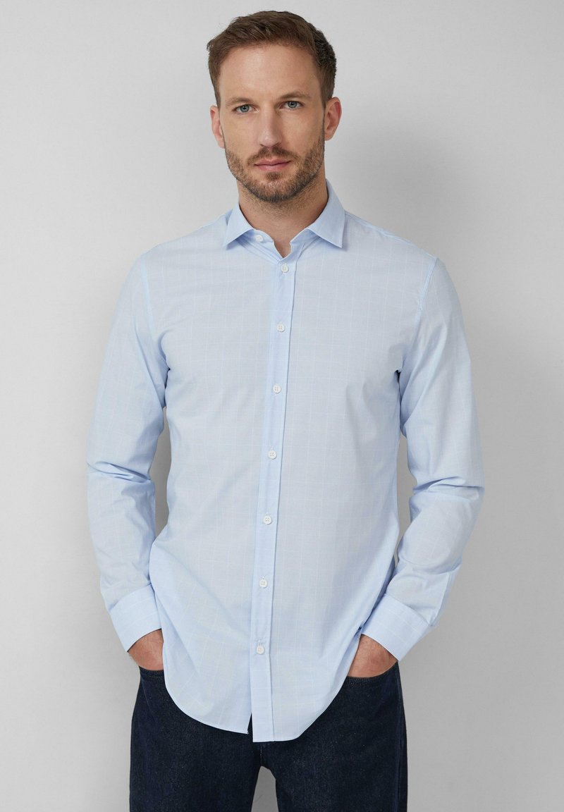 Chemise bleu clair à boutons avec de fines rayures verticales, à manches longues et col classique. Le tissu semble lisse avec une texture douce.
