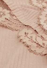 Lichtroze stof met ribbeltextuur en delicate kantafwerking, die gegolfde randen en ingewikkelde bloemenpatronen laat zien.