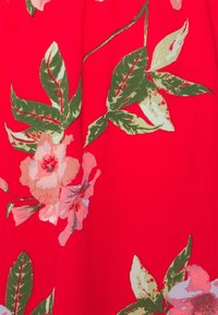 Tissu rouge avec un motif floral présentant des fleurs roses et des feuilles vertes. Le dessin est texturé avec des coutures visibles sur les pétales.