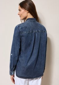 Donkerblauwe denim shirt met een zachte textuur, kraag, knopenmanchetten en een plooi aan de achterkant. Zijslitsen dragen bij aan het ontwerp.