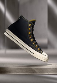 Zapatillas altas de lona azul marino, con ojales y costuras amarillas, suela de goma blanca y una clásica puntera redonda.