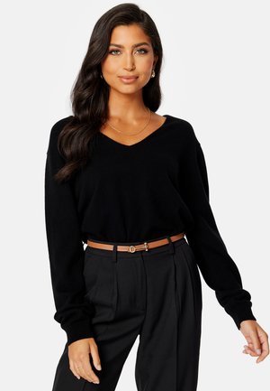 Maglione nero a scollo a V con maniche lunghe, abbinato a pantaloni neri su misura e una cintura marrone chiaro con una fibbia decorativa. Texture e vestibilità lisce.