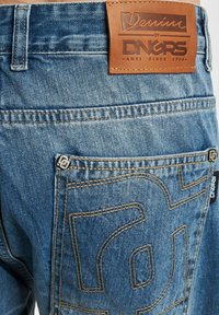 Denimjeans med blåvask, lærpatch med logo i livet, og et særegent brodert design på baklommen.