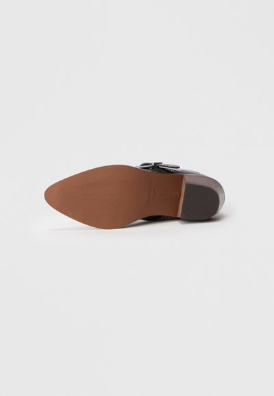 Brūnas ādas kurpes zole ar smailu pirkstu, ar gludu tekstūru un gaiši brūnu gumijas papēdi. Redzami metāla akcenti.