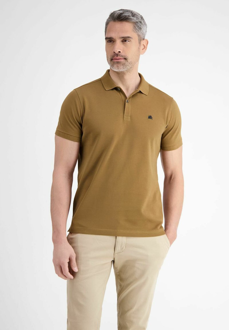 Korte mouwen polo shirt in mosterdgeel katoen met een zwart logo op de borst, gecombineerd met lichtbeige broeken. Gladde textuur.