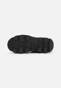 Suela de zapato de goma negra con un patrón de tracción texturizado, que presenta surcos y crestas profundas para mayor agarre, una plantilla plana y un diseño de punta redondeada.