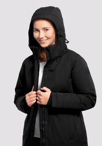Chaqueta impermeable negra con cremallera frontal y botones de presión, que cuenta con capucha y bolsillos laterales, hecha de un tejido suave y texturizado.