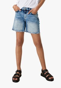 Džínové kraťasy světle modré barvy s vybledlým omakem, pět kapsový design a zapínání na knoflík. V kombinaci s černými sandály na pásky.