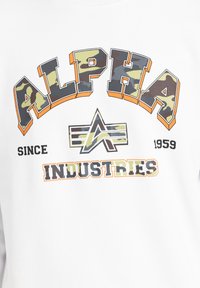 Felpa bianca con la scritta "ALPHA" in lettere audaci e camouflage multicolore, con "INDUSTRIES" sotto in nero, insieme a dettagli arancioni.