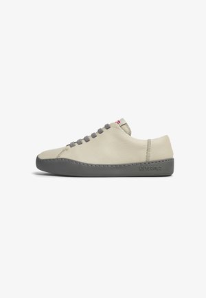 Zapatillas de cuero beige claro con suelas de goma gris, cordones texturizados y costuras en contraste. Logo en el lado lateral. Diseño plano.