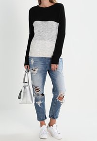 Czarny i szary sweter z kolorowymi blokami i prążkowanym dołem, zestawiony z podartymi jasnoniebieskimi dżinsami i białymi trampkami; trzymający srebrną torebkę.