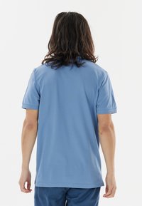 Vaaleansininen lyhythihainen polo-paita, joka on valmistettu pehmeästä kankaasta. Paidassa on tavallinen kaulus ja rento istuvuus, sekä siisti viimeistely helman osalta.