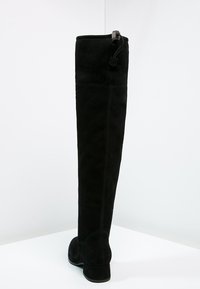 Botas de ante negras por encima de la rodilla con suela plana, punta redondeada, cremallera lateral y sutiles detalles de costura a lo largo de la parte posterior.
