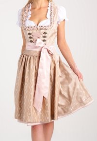 Tradycyjna bawarska sukienka dirndl w beżowym kolorze z kwiatowymi wzorami, różową satynową wstążką i koronkowymi akcentami. Posiada dopasowany gorset i rozkloszowaną spódnicę.