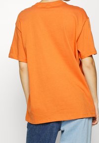 Överdimensionerad orange bomullströja med korta ärmar, rund halsringning och rak nederkant. Minimalistisk design, mjuk textur.