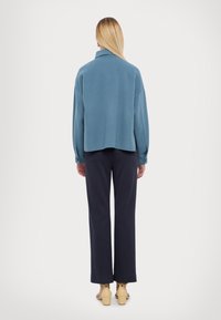 Maglione blu, oversize, con colletto e maniche lunghe, abbinato a pantaloni scuri. Le calzature presentano un tacco spesso di colore chiaro.