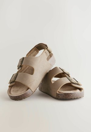 Beige sandaler med to justerbare spænder, åben design, blødt ruskindsmateriale, tekstureret indersål og en kraftig spraglet sål.