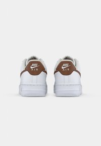 Par bijelih Nike Air tenisica prikazanih s leđa, s smeškastim petama i bijelim Nike logom i tekstom na svakoj peti.