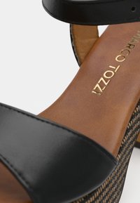 Μαύρη δερμάτινη σαγιονάρα με καφέ υφασμάτινη εσωτερική σόλα, πλεκτό στοιχείο και κομψό σχεδιασμό με χρυσή λεπτομέρεια στο λογότυπο.