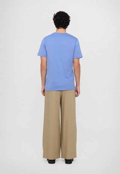 T-shirt en coton bleu à manches courtes, associé à un pantalon large beige. Texture lisse et design simple, vu de dos.