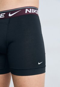 Crne atletske bokserice s bordo pojasom na kojem se nalazi Nike logo u bijeloj boji. Glatka tkanina s kontrastnim šavovima.