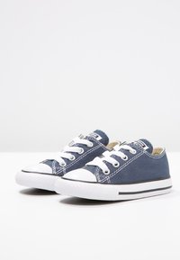 Granatowe trampki z płótna z białym gumowym czubkiem i podeszwą, wyposażone w białe sznurowadła i kontrastowe przeszycia, o niskim profilu.