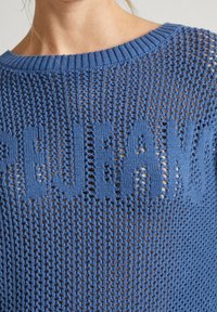 Niebieski sweter z dzianiny o luźnym, otwartym splotcie. Posiada duże litery wplecione w materiał. Wykończony okrągłym dekoltem.