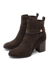 Botine din suede maro, cu toc înalt și pătrățos, vârf rotund și o curea laterală cu un buton decorativ. Textură netedă cu detalii de cusătură.