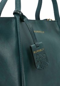 Borsa in pelle verde scuro con manici corti, targhetta in rilievo con logo leopardato e scritte dorate. Texture liscia e design strutturato.
