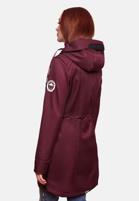 Burgundy waterproof jacket with a hood, drawstring, and a cinched waist. Features a logo patch on the sleeve and textured fabric.