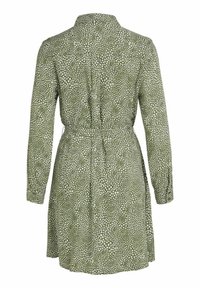 Grön långärmad klänning med vitt oregelbundet prickmönster, bälte i midjan och en lös, knälång kjol som visas från baksidan.