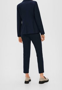 Navyblå kostymjacka med skräddarsydd passform och slag, matchad med smal passform på byxor och vardagsskor. Rent linjer och minimala detaljer.