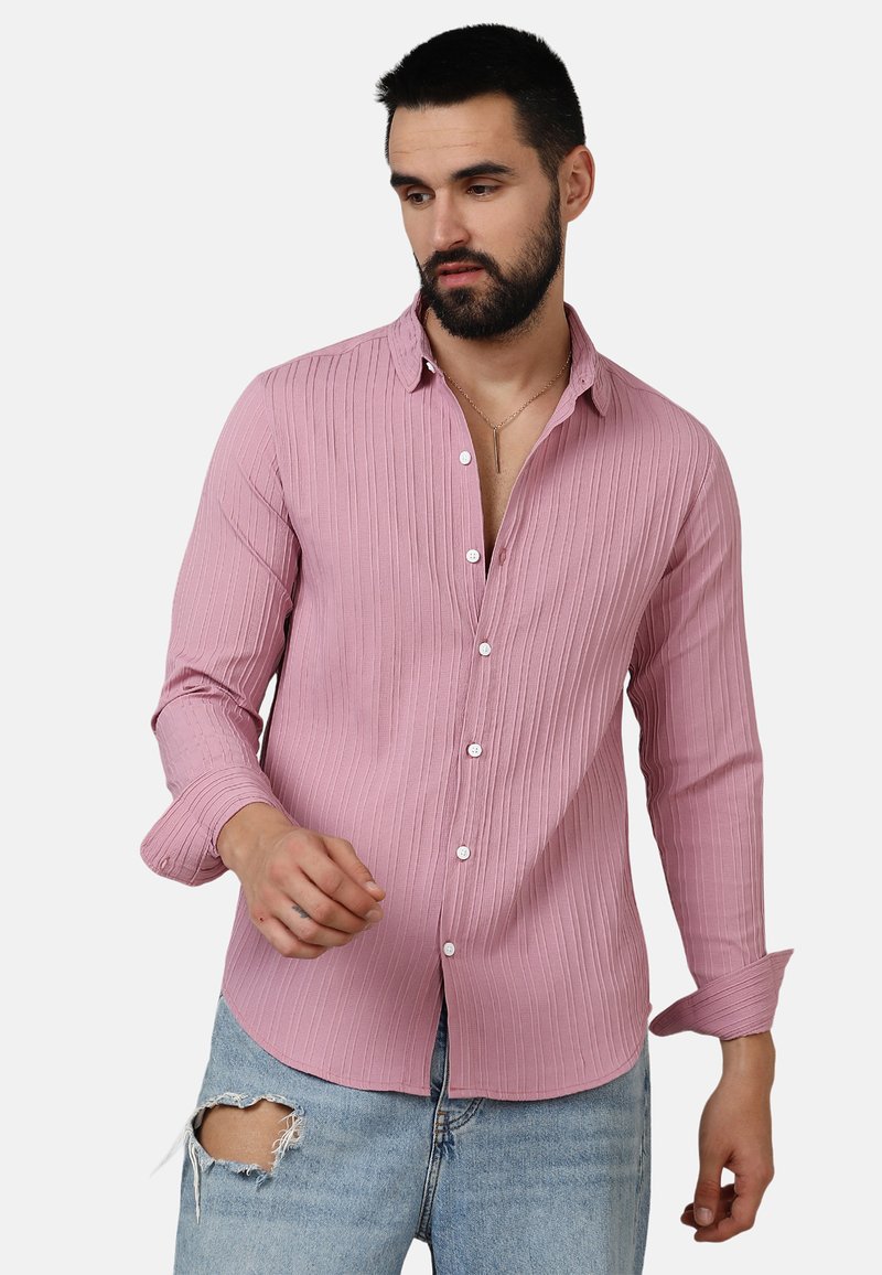 Camiseta de manga larga de color rosa claro, con canalé, cuello de solapa, botones en la parte frontal y mangas remangadas, combinada con jeans claros desgastados.