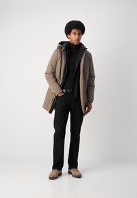Parka beige con capucha, suéter negro de cuello alto, pantalones negros y zapatos color beige. Textura suave, longitud media, cremallera frontal y bolsillos laterales.